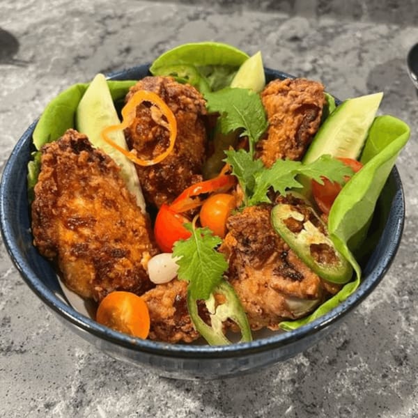 Crispy fried chicken pieces with fresh lettuce, cucumber, tomatoes, and jalapeños in a blue bowl.