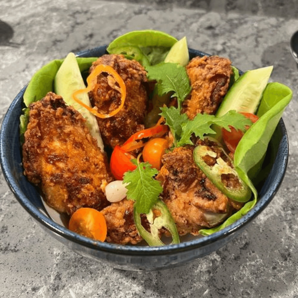 Crispy fried chicken pieces with fresh lettuce, cucumber, tomatoes, and jalapeños in a blue bowl.