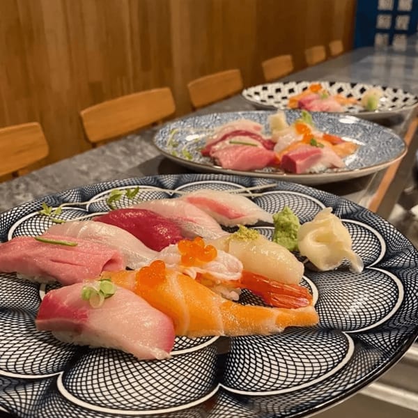 Plates of colorful nigiri sushi and sashimi with wasabi and ginger on a restaurant counter.